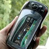 Schwarzes Handheld-Autorennspiel mit durchsichtigem Bildschirm, der eine Straße und kleine Autos zeigt, in einer Hand im Freien gehalten Produktbild-Vorschau