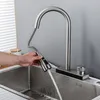 A hand is shown using a pull-down kitchen faucet over a stainless steel sink. Podgląd zdjęcia produktu