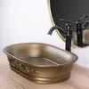 A close-up shot of a bronze vessel sink with ornate detailing, a dark bronze faucet, and a gold-rimmed mirror in the background, all placed on a wooden surface. Náhľad obrázku produktu