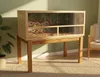 A terrarium on a wooden stand in a room with a plant and a chair. Produktbild-Vorschau