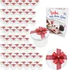 A collection of small glass jars with red ribbon bows, a recipe book, and a decorative plate, all presented on a white background. Produktbild-Vorschau
