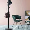 A coat rack with a handbag and hat is shown next to a green chair in a room with a pink wall and blue carpet. Produktbild-Vorschau