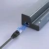 A close-up of a USB-C hub adapter with an Ethernet cable being plugged into it, with blue light effects indicating data transfer. Produktbild-Vorschau