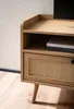 A close-up view of a wooden TV stand with a rattan drawer front. Produktbild-Vorschau