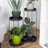 Two black metal plant stands with plants in pots, placed on a wooden floor next to a sofa and a white shelf. Produktbild-Vorschau