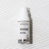A white pump bottle of serum is placed on a textured white surface. Produktbild-Vorschau