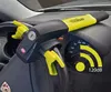 A car steering wheel lock with an alarm system is attached to the steering wheel of a car, with the dashboard and speedometer visible in the background. Voir les images du produit