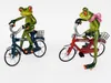 Two decorative frog figurines riding bicycles. Produktbild-Vorschau