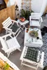 An outdoor patio setting with white wooden chairs and tables, decorated with plants and a surfboard. Náhled obrázku produktu