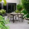 An outdoor patio setting with a dining table and chairs surrounded by lush greenery and flowers. Anteprima dell’immagine prodotto