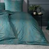 A close-up view of bedding on a bed, with a small side table and decor in the background. Produktbild-Vorschau