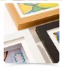 Three picture frames with different colored borders (wood, black, and white) are shown from a close-up angle, with parts of children's artwork visible inside the white and black frames. Produktbild-Vorschau