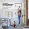 A woman is stretching on a wooden climbing wall in a child's bedroom, while a young girl sits on the floor in front of her. Voir les images du produit