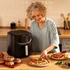 A woman is in a kitchen, preparing food next to an air fryer. There are pastries and a pizza on the counter. Produktbild-Vorschau