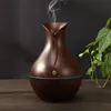 A dark wood-grain aroma diffuser emitting a stream of vapor, placed on a wooden surface with a plant in the background. Produktbild-Vorschau