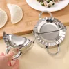 Two stainless steel dumpling makers are shown on a wooden surface, with some uncooked dumplings and filling in the background. Produktbild-Vorschau