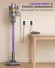 A purple and gray cordless vacuum cleaner is shown mounted on a wall charger, with two charging cables plugged into wall outlets. A table is visible on the right side of the image. Produktbild-Vorschau
