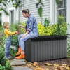 A woman and a child are in a garden setting, with the child handing a plant to the woman who is sitting on a storage box. Voir les images du produit