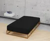 A black mattress on a wooden bed frame against a concrete wall. Produktbild-Vorschau