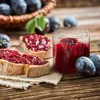 A rustic scene with plum jam on toast, a jar of jam, and plums on a wooden table. Voir les images du produit