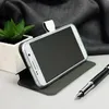 A smartphone in a flip case is propped up on a desk, next to a small plant and a pen. Produktbild-Vorschau