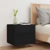 A black floating nightstand with two drawers is shown next to a bed with a wooden headboard. A vase with a plant and a small clock on top of books are on the nightstand. Náhľad obrázku produktu