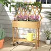 A wooden planter box with flowers and vines sits on a deck, with a watering can and trowel on the shelf below. Produktbild-Vorschau