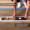 A person is assembling a white desk frame on a wooden floor. Produktbild-Vorschau