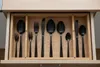 A cutlery drawer with black utensils neatly organized in wooden compartments. Náhled obrázku produktu