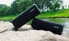 Two black speakers are placed on rocks next to a body of water with trees in the background. Náhled obrázku produktu