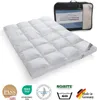 A white down comforter is laid out flat, with a black carrying bag in the background. Several certification logos are visible at the bottom. Produktbild-Vorschau