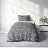A bed with geometric patterned bedding is shown in a room with a white brick wall and a floor lamp. Produktbild-Vorschau