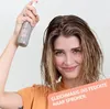A woman is holding a spray bottle and applying it to her hair. Produktbild-Vorschau