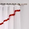 A close-up view of a white sheer curtain with a red ribbon trim, hanging from a curtain rod. Produktbild-Vorschau