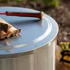 A close-up shot of a metal lid with firewood and a tool on top, set outdoors. Produktbild-Vorschau