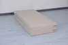 A folded beige gymnastics mat is placed on a light gray floor in front of a white wall. Náhled obrázku produktu