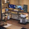 A modern L-shaped gaming desk setup with multiple monitors, a laptop, and accessories, illuminated by LED lighting. Produktbild-Vorschau