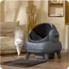 A white cat is walking past an automatic cat litter box in a living room setting. Anteprima dell’immagine prodotto