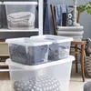Several transparent storage boxes filled with folded clothes and bedding are stacked on shelves, with a chair and decorative items in the background. Voir les images du produit