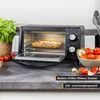 A toaster oven with a pizza inside, on a countertop with ingredients. Voir les images du produit