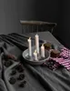 A table set with a grey tablecloth, a candle holder with lit candles, pinecones, and cookies. Produktbild-Vorschau