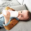 A baby lying on a couch and drinking from a bottle. Produktbild-Vorschau