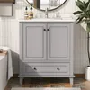 A gray vanity cabinet with two doors and a drawer, featuring a white countertop and a modern faucet. The background includes white subway tiles and a plant. Podgląd zdjęcia produktu