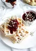 A close-up of waffles with jam and powdered sugar, decorated with small white flowers. Anteprima dell’immagine prodotto