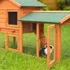 A rabbit is inside a wooden hutch with a green roof, placed on green grass. Produktbild-Vorschau