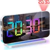 A digital alarm clock with a mirrored surface displaying the time and reflecting a living room scene. A red projection of the time is visible on the ceiling. Produktbild-Vorschau