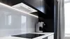 A modern kitchen scene with a sleek white range hood over a black induction stovetop. A silver espresso machine sits on the white countertop. Produktbild-Vorschau
