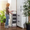 A woman is using a step stool next to a tall cabinet in a room with plants. Podgląd zdjęcia produktu