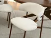 A close-up view of two beige upholstered dining chairs with walnut-colored legs, placed on a light gray rug next to a wooden dining table. Voir les images du produit