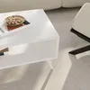 A white coffee table with a book and nuts on it, next to a beige chair in a living room. Podgląd zdjęcia produktu
